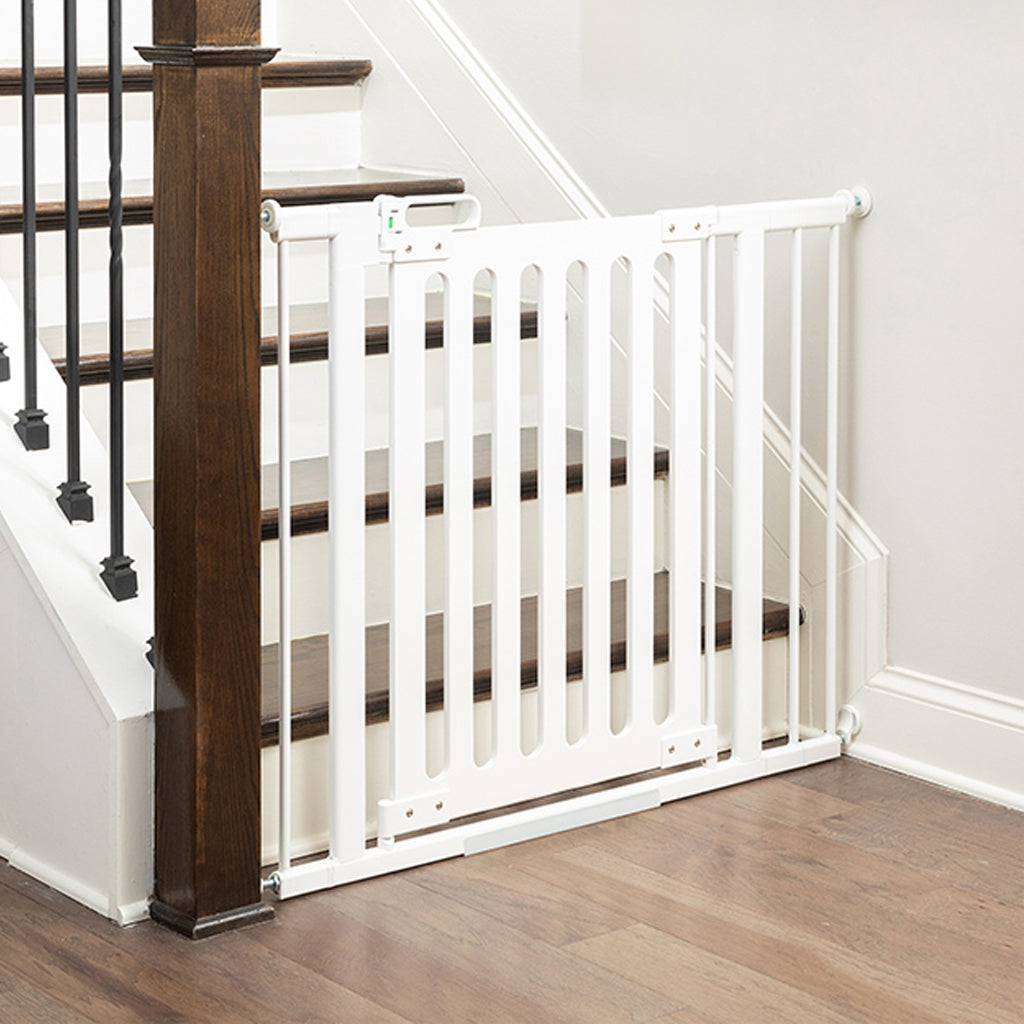 A white baby stair gate installed across wooden stairs next to a dark wood banister post.